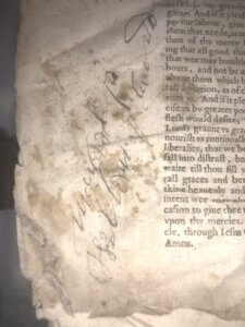 A close-up of an old, stained manuscript page with handwritten cursive notes in pencil on the left margin and printed text on the right. The edges of the page appear worn and torn.