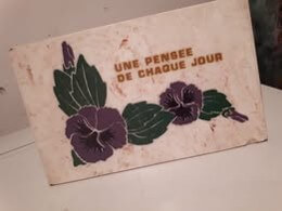 A card with purple flowers and green leaves reads “UNE PENSÉE DE CHAQUE JOUR” in gold text, placed on a white surface.