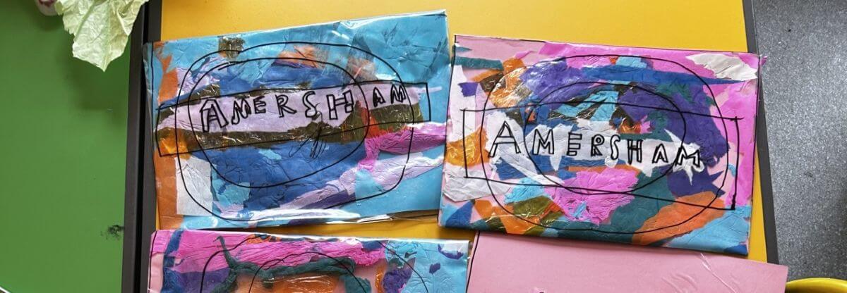Three colourful collages with overlapping paint and paper feature the word AMERSHAM outlined in black. The backgrounds are blue, pink, and multicoloured, and the artworks are spread out on a table.
