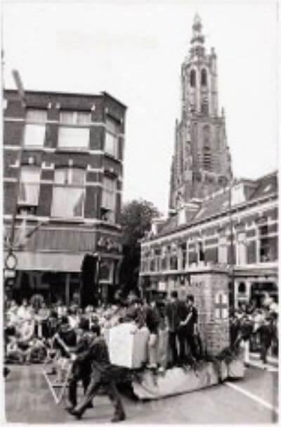 Black-and-white historical photograph shows a crowded street parade and a decorated float
